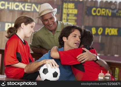 Mid adult man hugging his son in a restaurant with his father and daughter looking at them