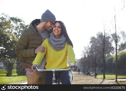 Mid adult man hugging smiling mid adult woman on bicycle in park