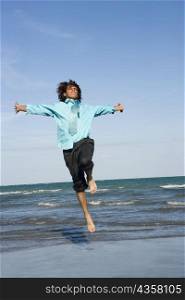 Mid adult man jumping on the beach with his arm outstretched