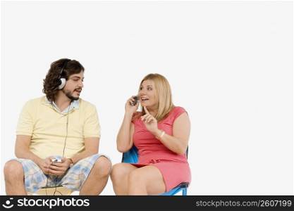 Mid adult man listening to music with a mature woman sitting beside him and talking on a mobile phone