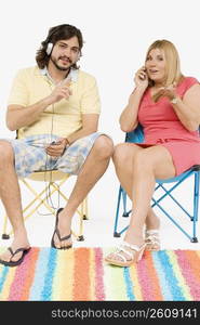 Mid adult man listening to music with a mature woman sitting beside him and talking on a mobile phone