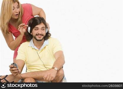 Mid adult man listening to music with a mature woman standing behind him and playfully touching his headphones