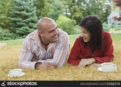 Mid adult man lying in a lawn with a mature woman and smiling