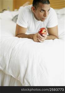 Mid adult man lying on the bed and holding an apple