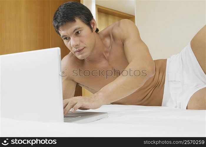 Mid adult man lying on the bed and using a laptop