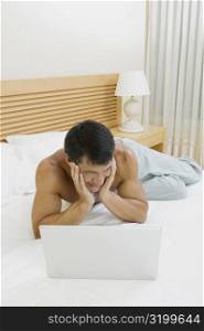 Mid adult man lying on the bed with a laptop in front of him