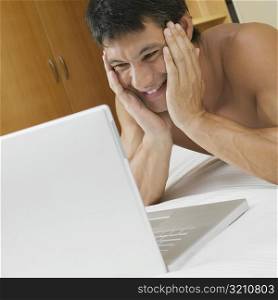 Mid adult man lying on the bed with a laptop in front of him