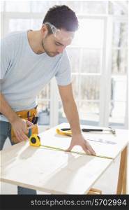 Mid-adult man marking table with measure tape