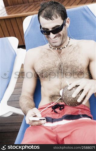 Mid adult man reclining on a lounge chair and listening to music on an MP3 player