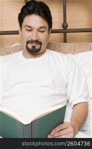 Mid adult man reclining on the bed and reading a book