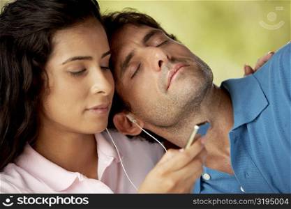 Mid adult man resting on a young woman&acute;s shoulder and listening to music