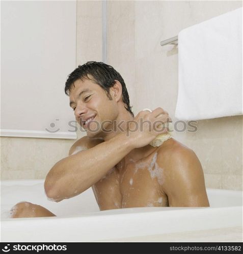 Mid adult man scrubbing his body in the bathtub