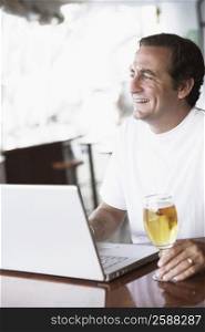 Mid adult man sitting in front of a laptop and holding a glass of beer