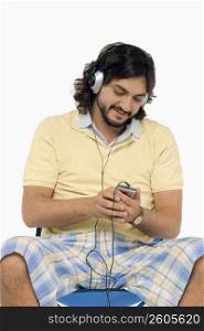 Mid adult man sitting on a stool and listening to an Mp3 player