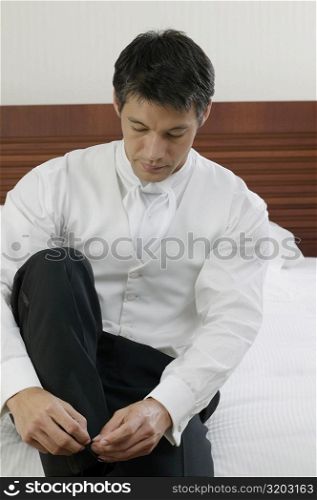 Mid adult man sitting on the bed and tying his shoelaces