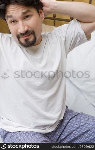 Mid adult man sitting on the bed with his hands behind his back