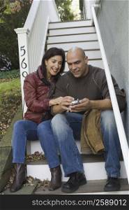 Mid adult man sitting with a mature woman and operating a mobile phone