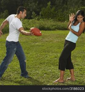 Mid adult man standing holding a football in front of a young woman