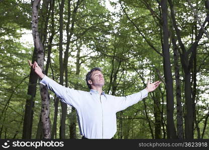 Mid adult man standing in forest with outstretched arms and closed eyes