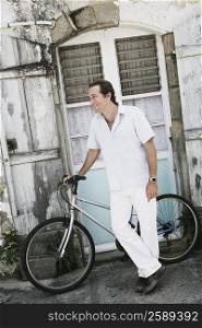 Mid adult man standing near a bicycle in front of a house