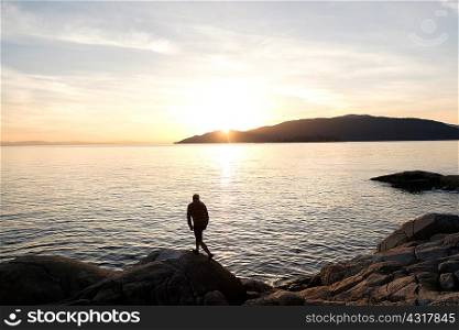 Mid adult man standing on rock, looking at view across lake, rear view