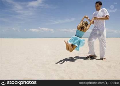 Mid adult man swinging her daughter on the beach
