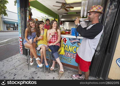 Mid adult man taking a photograph of a teenage girl and her three friends