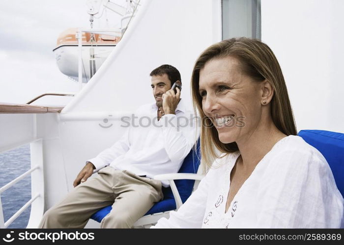 Mid adult man talking on a mobile phone with a mid adult woman sitting on a chair and smiling