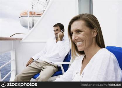 Mid adult man talking on a mobile phone with a mid adult woman sitting on a chair and smiling