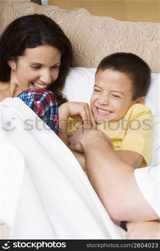 Mid adult man tickling his son with a mid adult woman lying beside them
