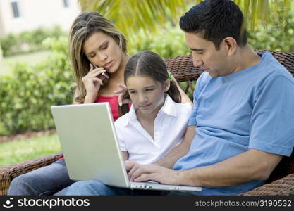 Mid adult man using a laptop with a girl and a young woman sitting beside them