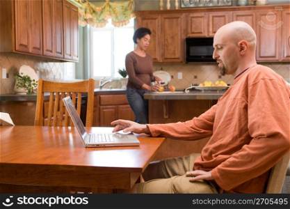 Mid adult man using laptop while mid adult woman cutting fruits