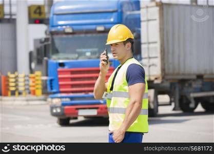 Mid adult man using walkie-talkie in shipping yard