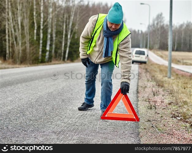 Mid adult man wearing reflector vest and he have a red warning triangle - road and vehicle on background