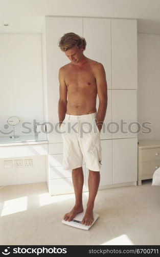 Mid adult man weighing himself on a weighing scale