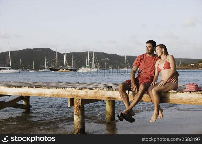Mid adult man with his arm around a mid adult woman and sitting on a jetty