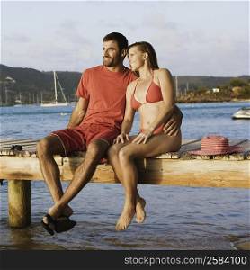 Mid adult man with his arm around a mid adult woman and sitting on a jetty