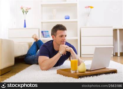 Mid-adult man working on laptop computer at home, lying on floor.