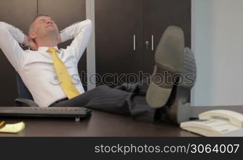 Mid- adult manager relaxing at work with feet on desk