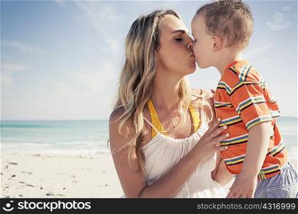 Mid adult mother kissing young son on beach, Cape Town, Western Cape, South Africa