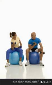 Mid adult multiethnic man and woman balancing on blue exercise balls while working out with dumbbells.