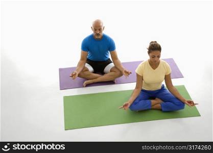 Mid adult multiethnic man and woman sitting in lotus position on exercise mats with eyes closed and legs crossed.