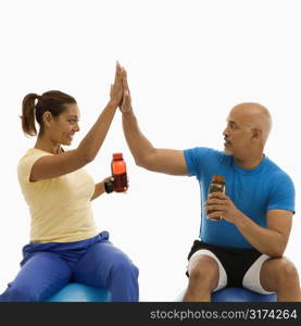 Mid adult multiethnic man and woman sitting on blue exercise balls giving each other the high five.