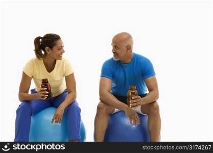 Mid adult multiethnic man and woman sitting on blue exercise balls looking at each other.