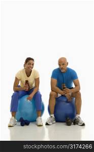 Mid adult multiethnic man and woman sitting on blue exercise balls taking a break.