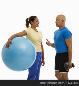 Mid adult multiethnic woman holding blue exercise ball standing with mid adult multiethnic man looking at each talking.