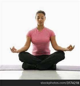 Mid adult multiethnic woman sitting in lotus position on exercise mat with eyes closed and legs crossed.