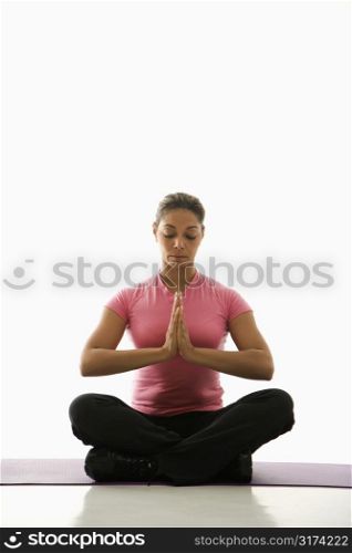 Mid adult multiethnic woman sitting in Namaste position on exercise mat with eyes closed and hands at heart center.