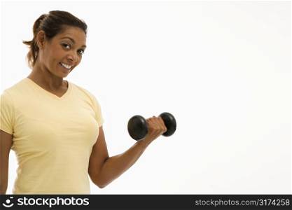 Mid adult multiethnic woman wearing yellow exercise shirt doing arm curls looking at viewer and smiling.