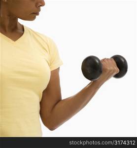 Mid adult multiethnic woman wearing yellow exercise shirt doing arm curls looking at bicep.